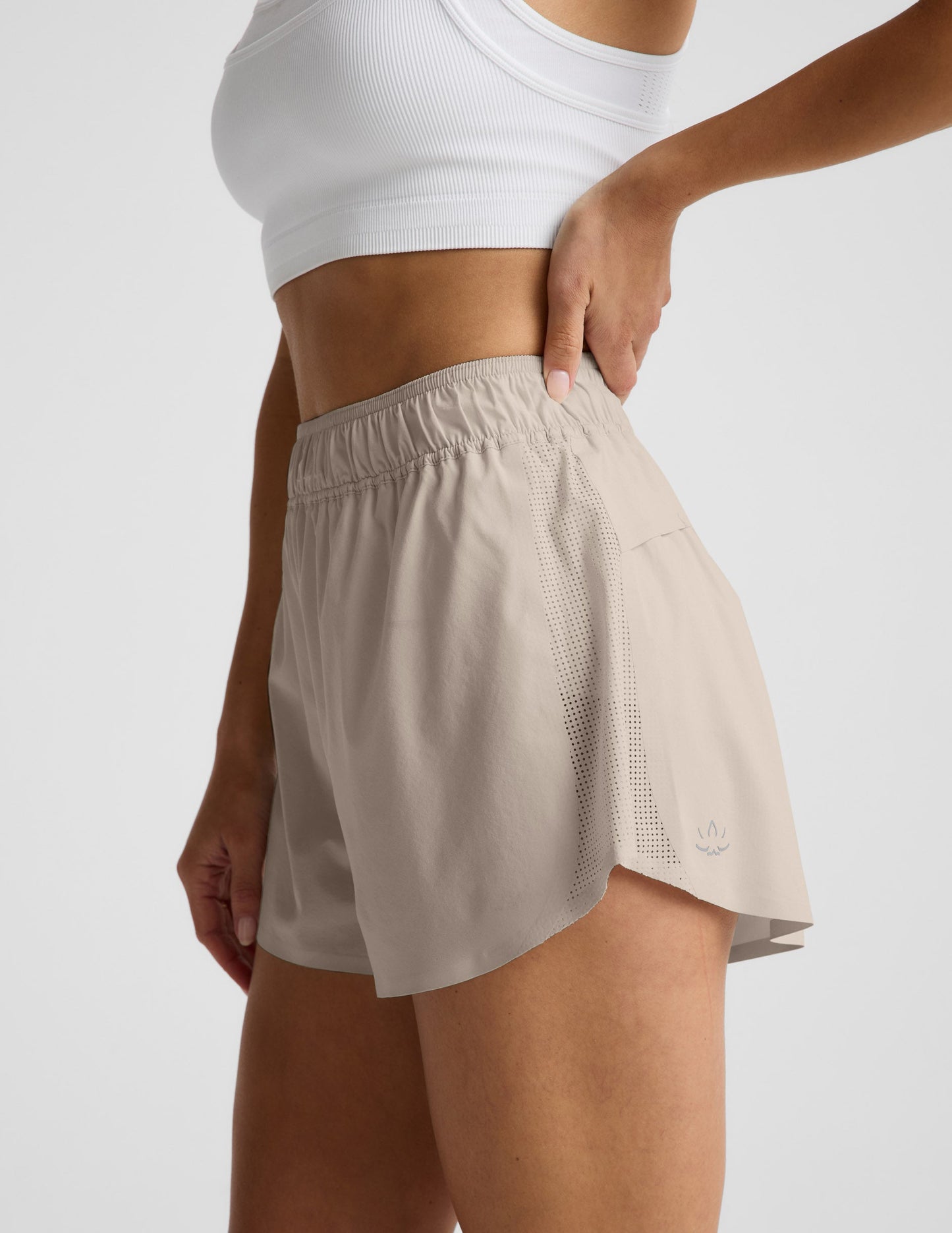 Woman wearing Beige Solemate™ 2.5" Short in a side profile, paired with a white sports bra, featuring perforated panels.