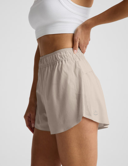 Woman wearing Beige Solemate™ 2.5" Short in a side profile, paired with a white sports bra, featuring perforated panels.