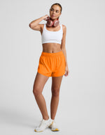 Woman wearing Orange Solemate™ 2.5" Short with a gathered elastic waistband, paired with a white sports bra and sneakers.