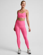 Woman wearing a pink bra and 7/8 length high waisted leggings against a plain background.