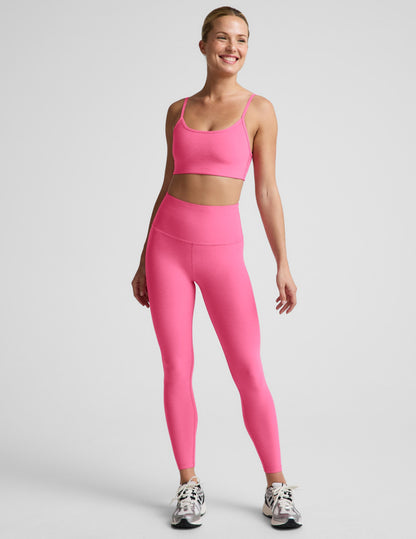 Woman wearing a pink bra and 7/8 length high waisted leggings against a plain background.