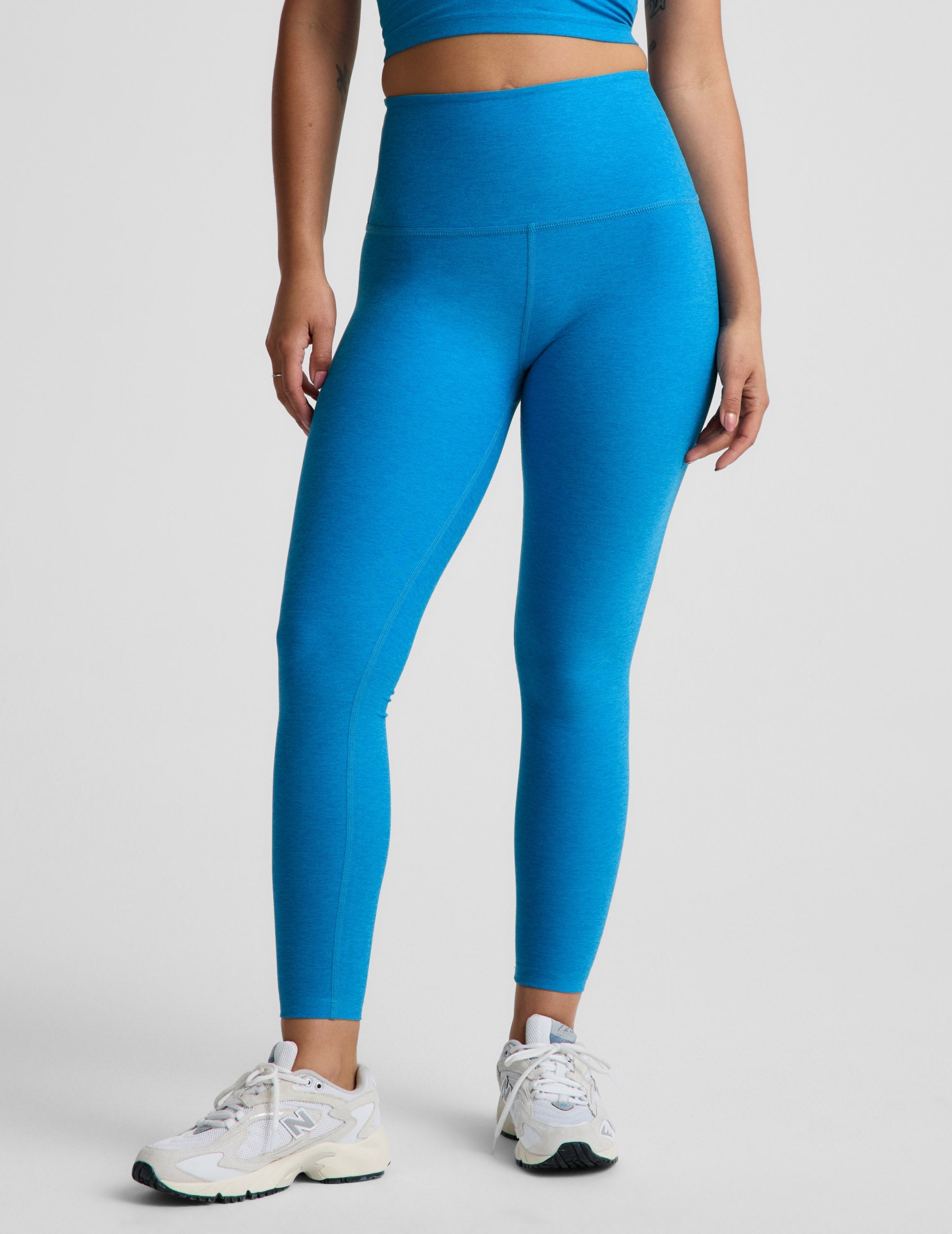 Woman wearing a blue cropped tank top and blue high-waisted midi leggings against a plain background.