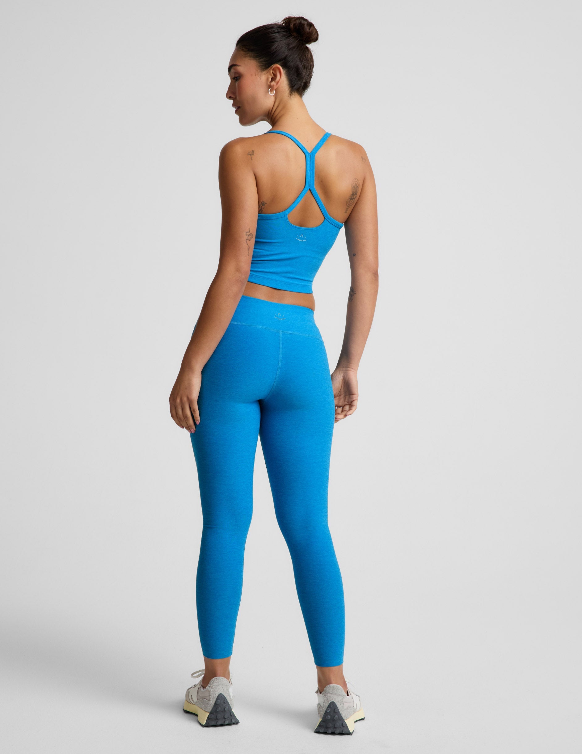 Woman wearing a blue cropped tank and blue mid-rise leggings against a plain background.