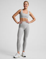 Woman wearing a gray sports bra and leggings with white contrast piping on a plain background.
