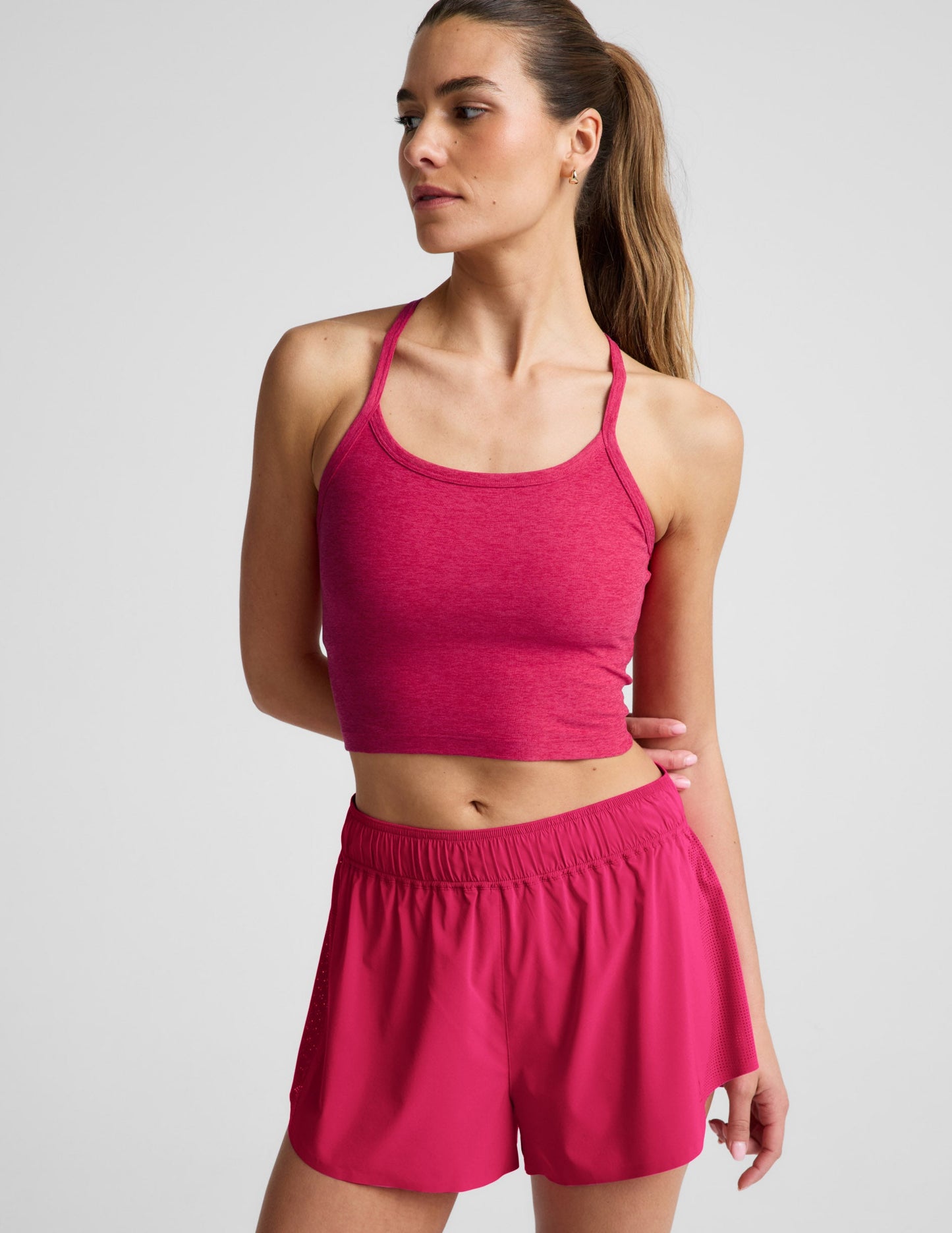 Woman is wearing a red cropped tank and red athletic shorts against a light gray background.