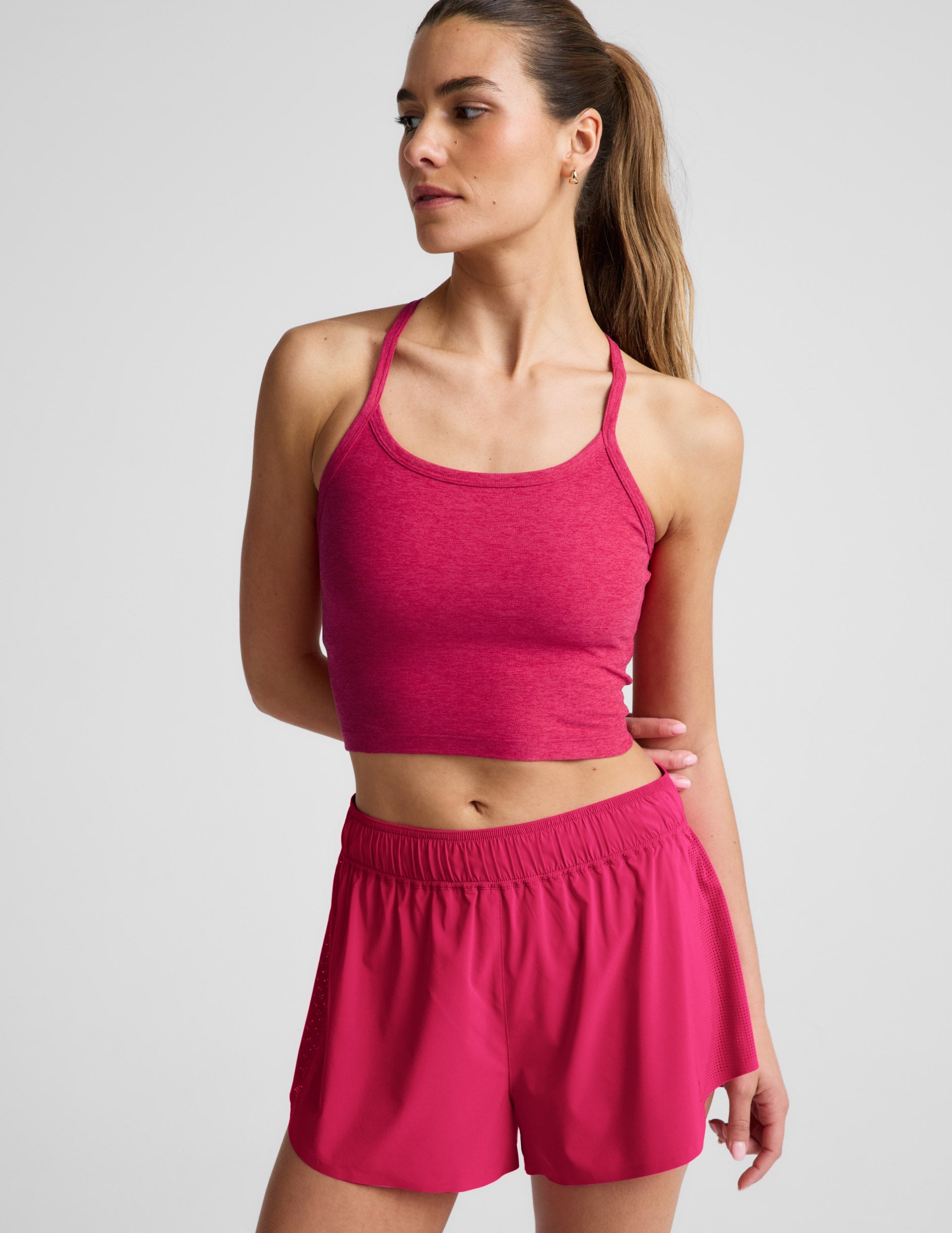 Woman is wearing a red cropped tank and red athletic shorts against a light gray background.