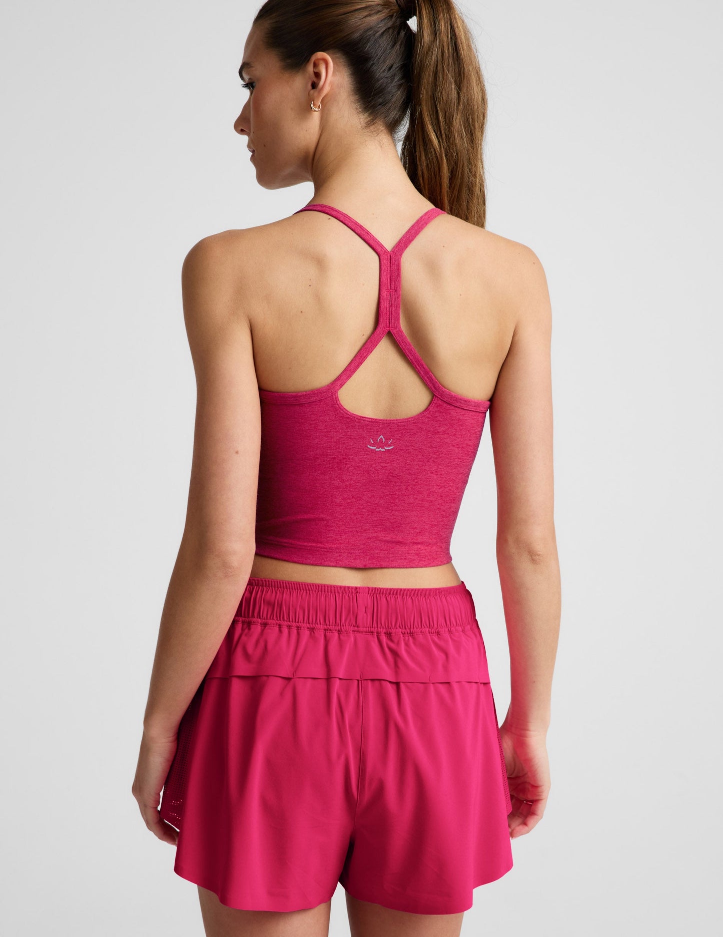 Woman is wearing a red cropped tank and red athletic shorts against a light gray background.
