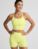 Woman wearing a bright yellow cropped racerback tank and biker shorts against a light gray background.