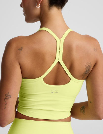 Woman wearing a bright yellow cropped racerback tank and biker shorts against a light gray background.