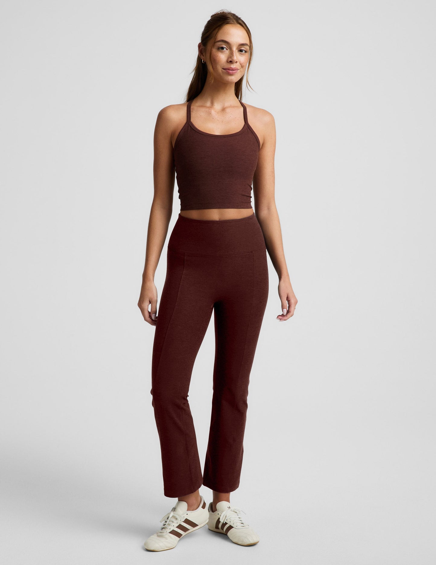 Woman wearing a brown racerback cropped tank top and brown high-waisted midi length leggings against a plain background.
