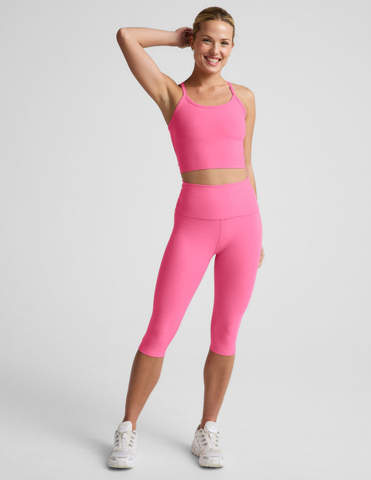 Woman wearing a pink cropped racerback tank top and leggings against a plain background.