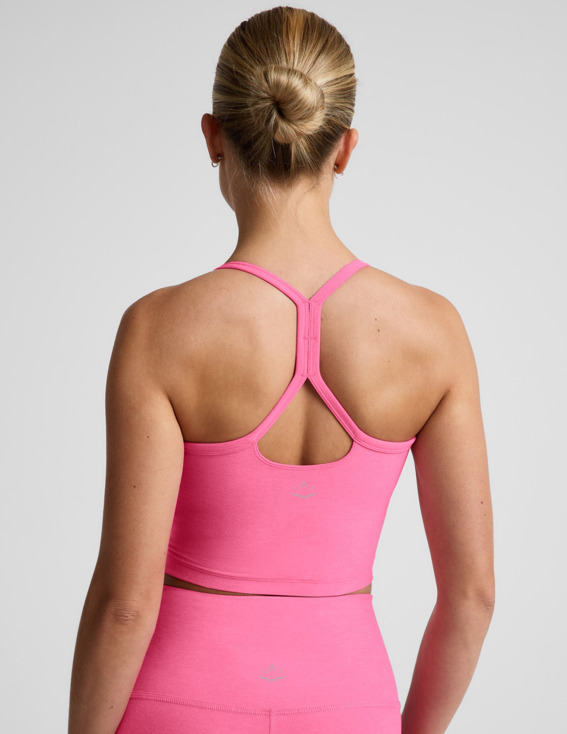 Woman wearing a pink cropped racerback tank top and leggings against a plain background.