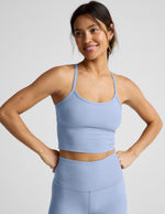 Woman wearing a blue cropped racerback tank and leggings against a plain background.