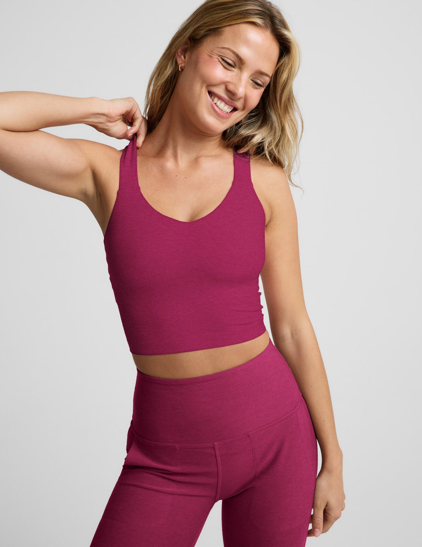 Woman wearing a red cropped tank with a twist cutout back detail and red pants against a plain background.