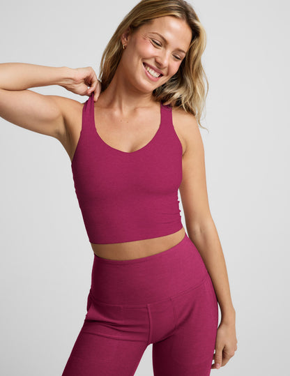 Woman wearing a red cropped tank with a twist cutout back detail and red pants against a plain background.