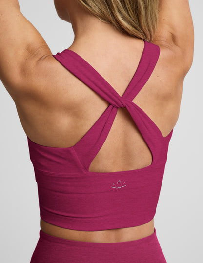 Woman wearing a red cropped tank with a twist cutout back detail and red pants against a plain background.
