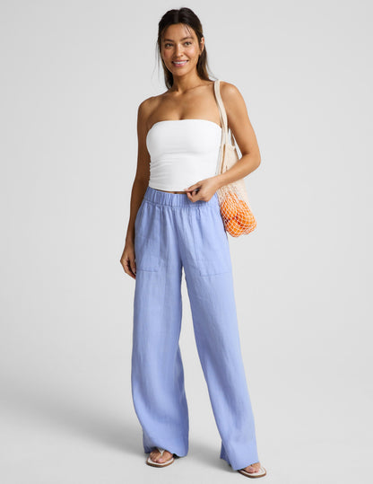 Woman wearing a white strapless top and blue pants against a plain background.