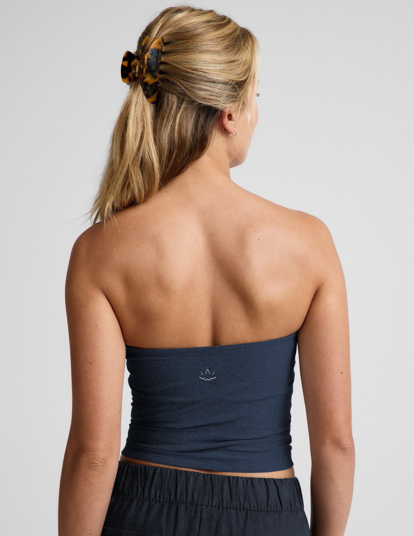 Woman wearing a navy strapless tank and navy linen pants against a plain background.
