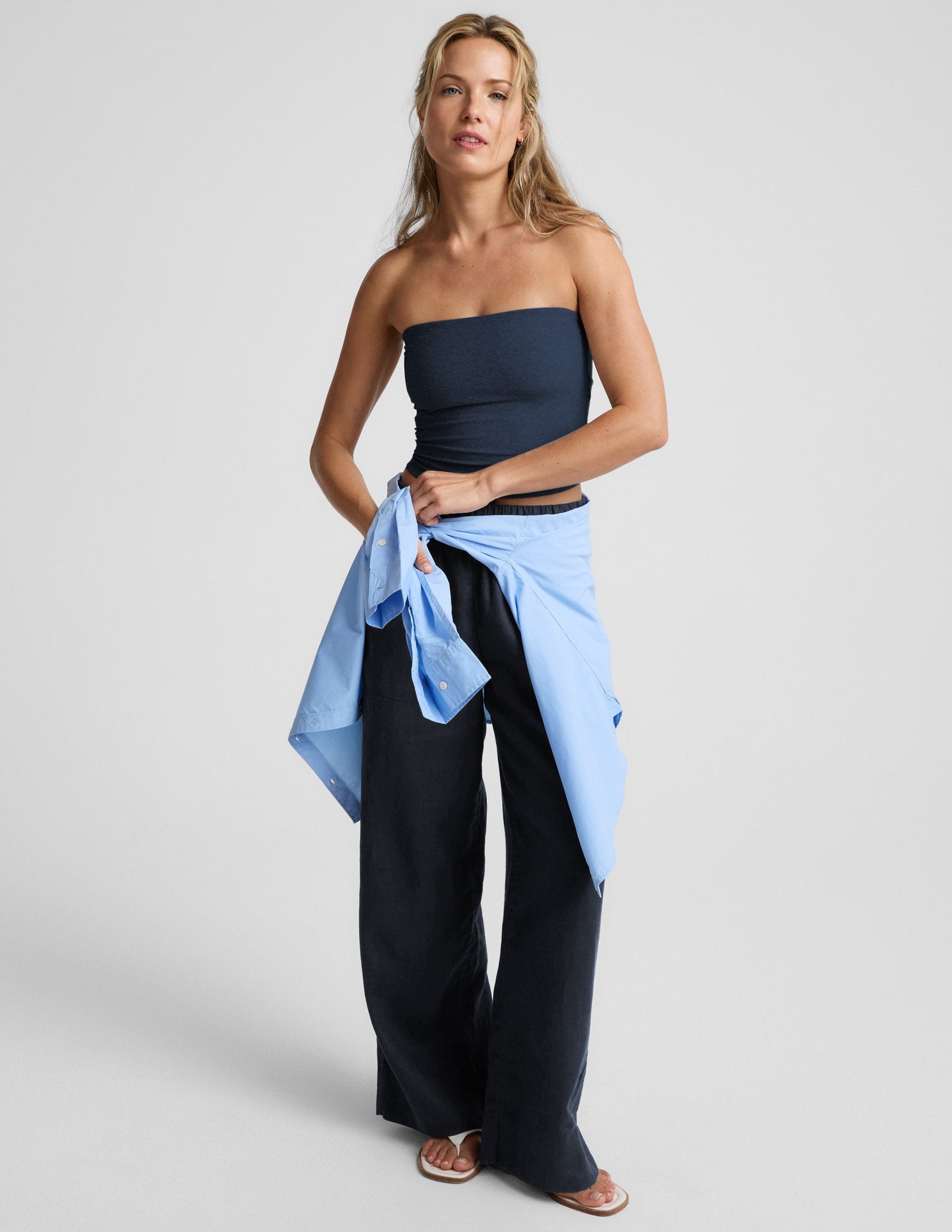 Woman wearing a navy strapless tank and navy linen pants against a plain background.