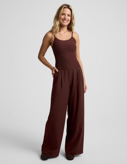 Woman wearing a brown waist length tank top and pants against a plain background.