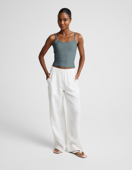 Woman wearing a green tank top and white pants against a plain background.