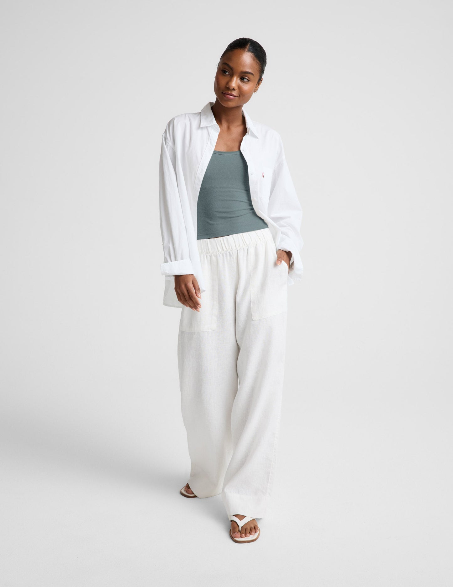 Woman wearing a green tank top and white pants against a plain background.