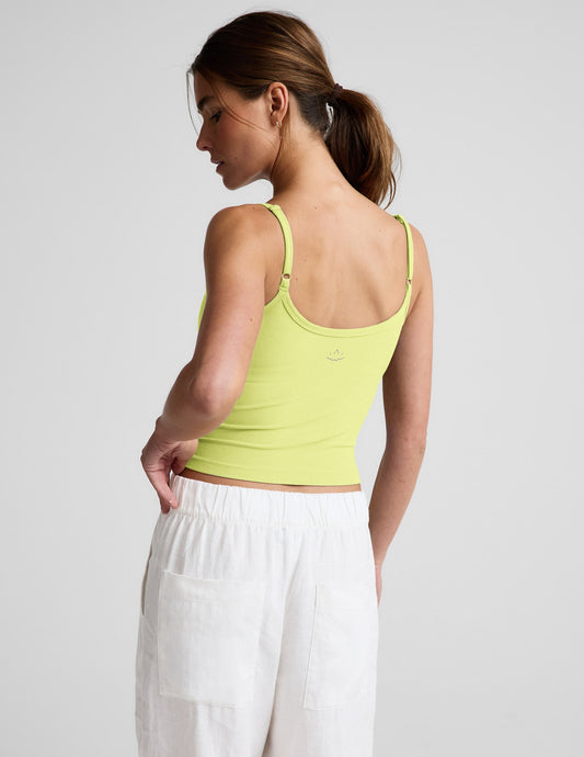 Woman wearing a yellow waist length tank and white linen pants against a plain background.