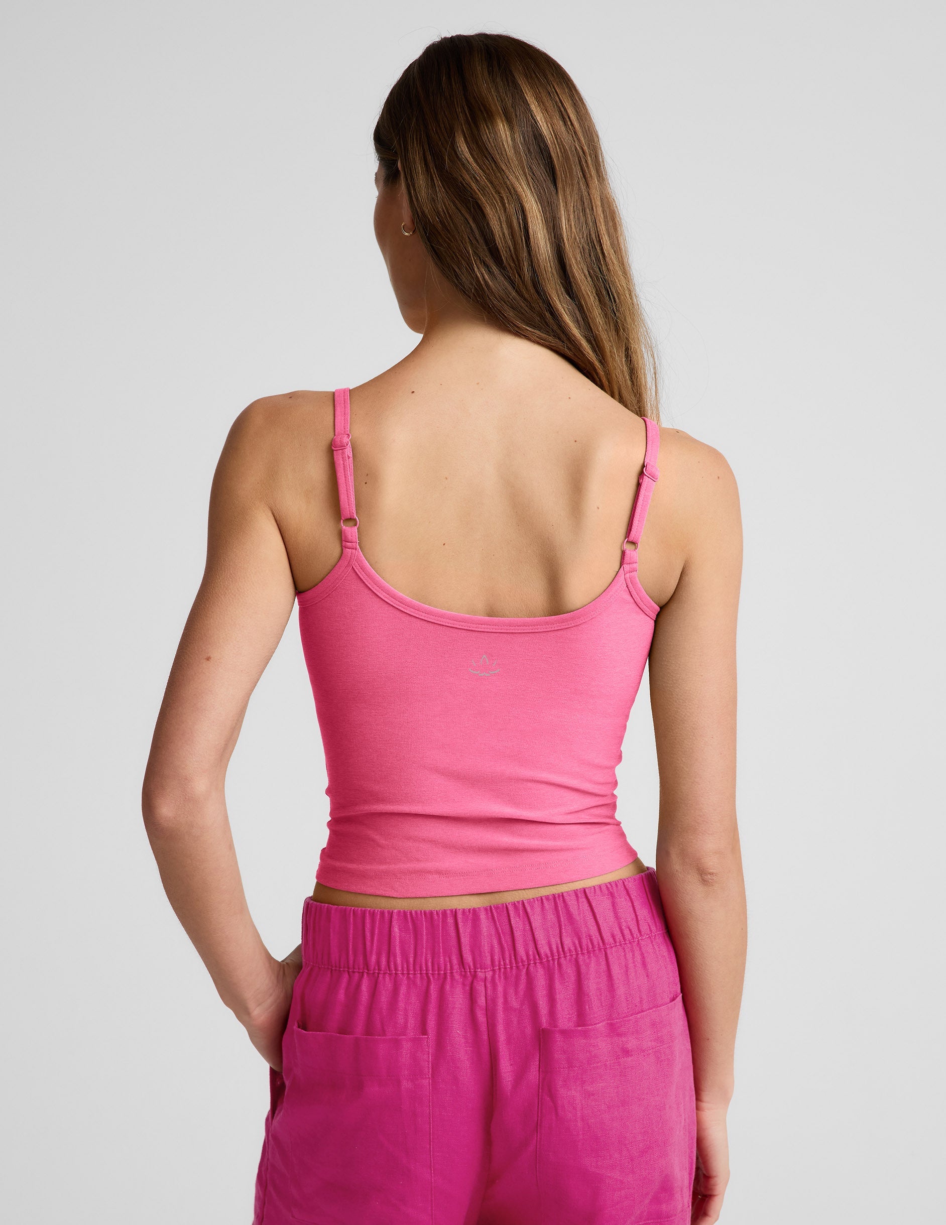 Woman wearing a pink waist length tank top and pink linen pants against a plain background.