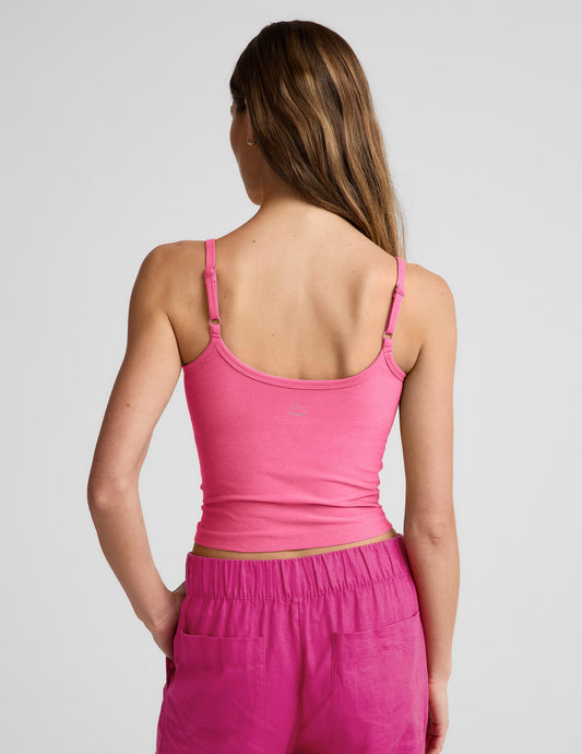 Woman wearing a pink waist length tank top and pink linen pants against a plain background.
