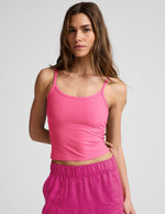 Woman wearing a pink waist length tank top and pink linen pants against a plain background.