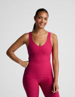 Woman wearing a red tank top and leggings on a light gray background.