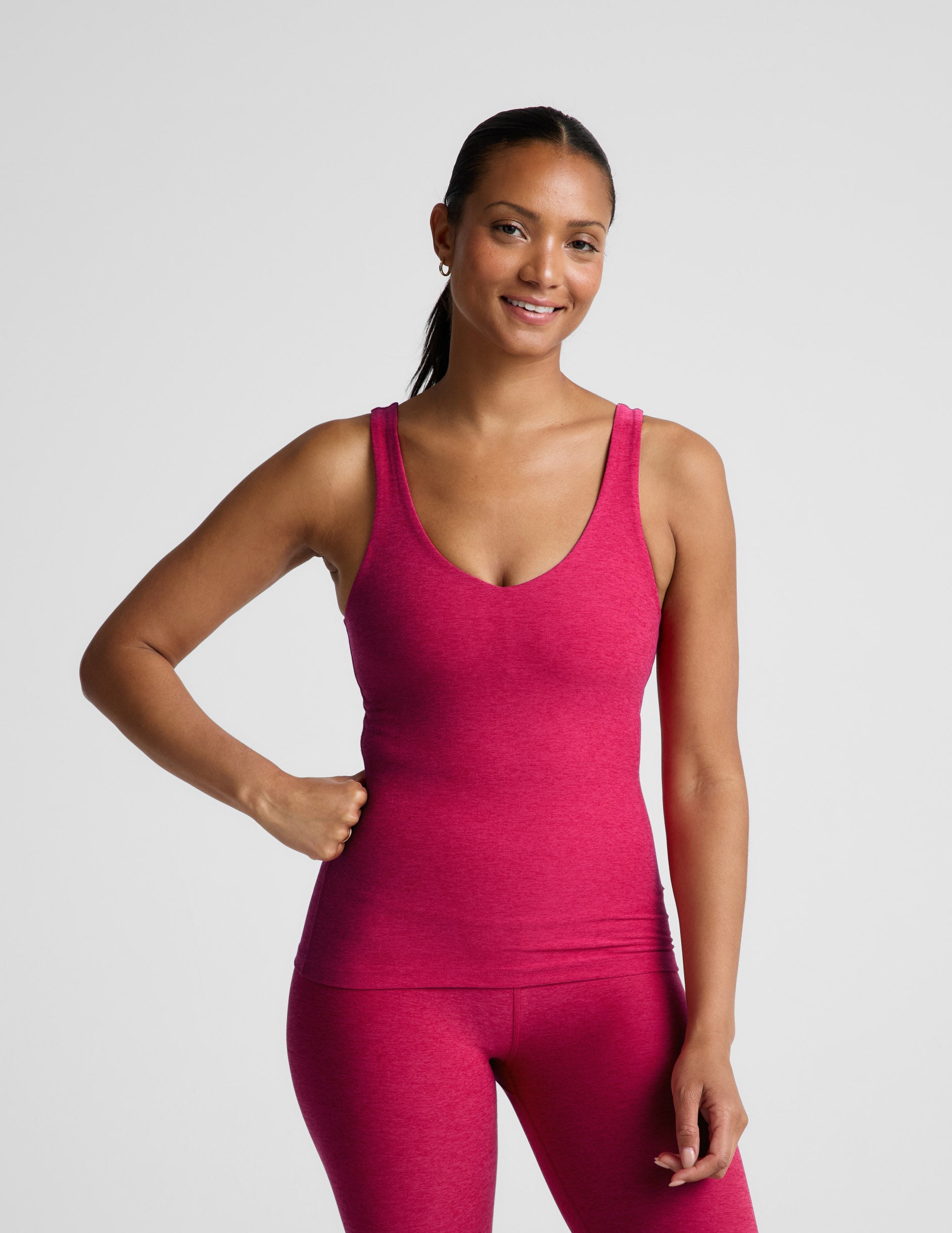 Woman wearing a red tank top and leggings on a light gray background.