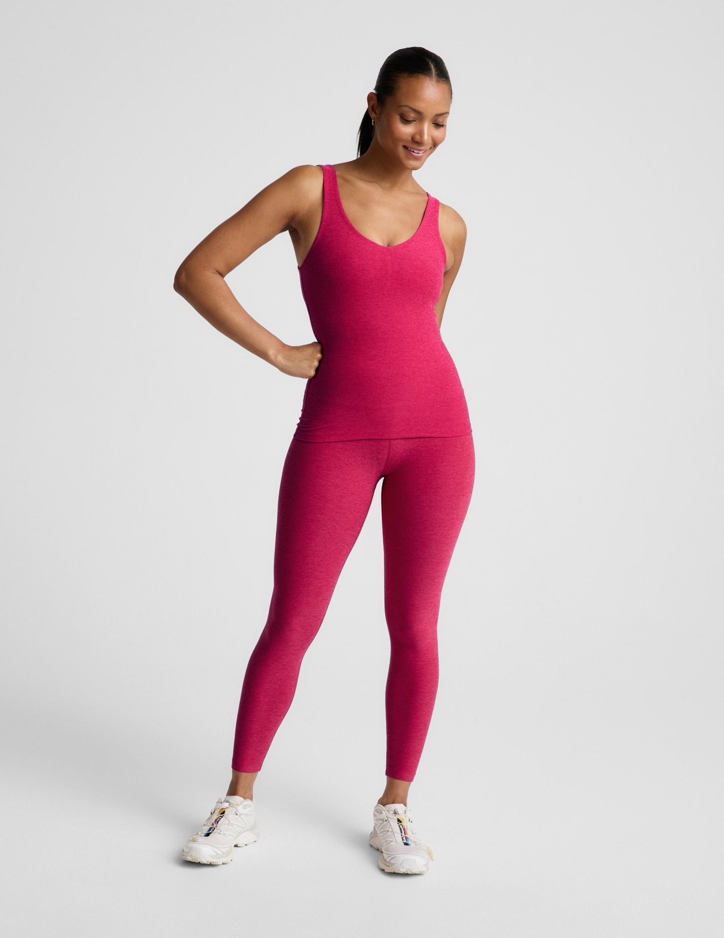 Woman wearing a red tank top and leggings on a light gray background.