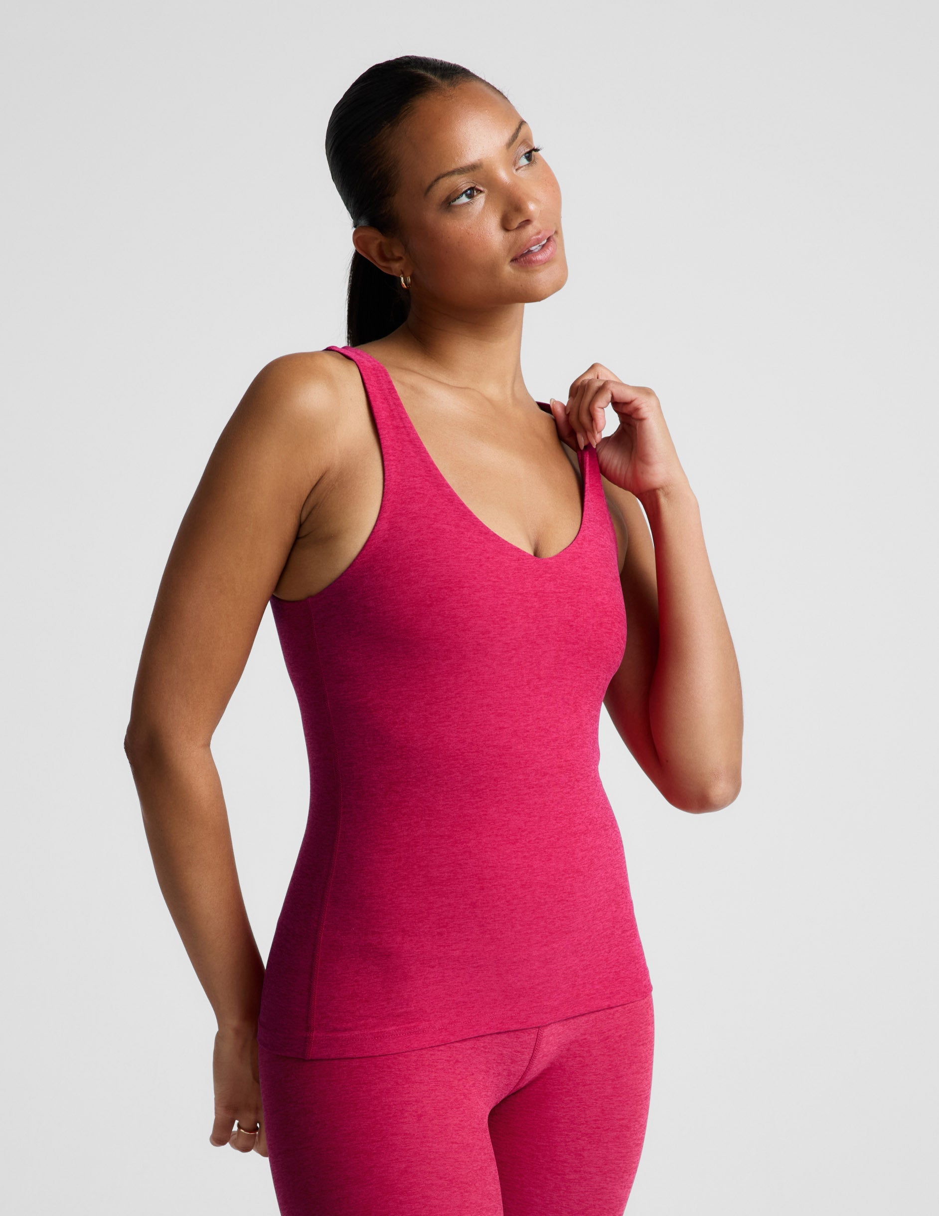 Woman wearing a red tank top and leggings on a light gray background.