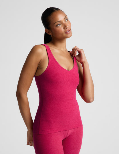 Woman wearing a red tank top and leggings on a light gray background.