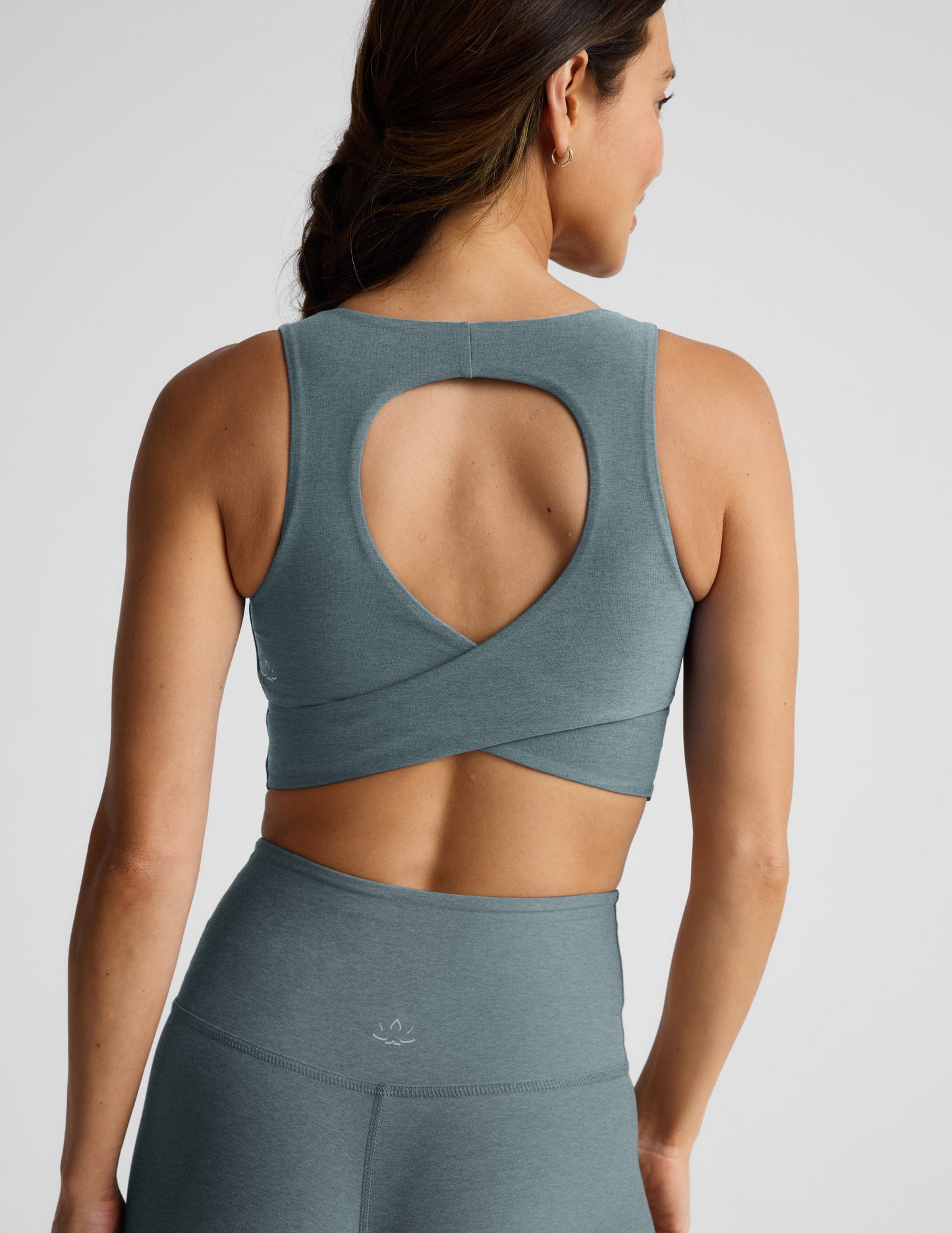 Woman wearing a green cropped tanks and leggings on a light gray background.