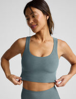 Woman wearing a green cropped tanks and leggings on a light gray background.