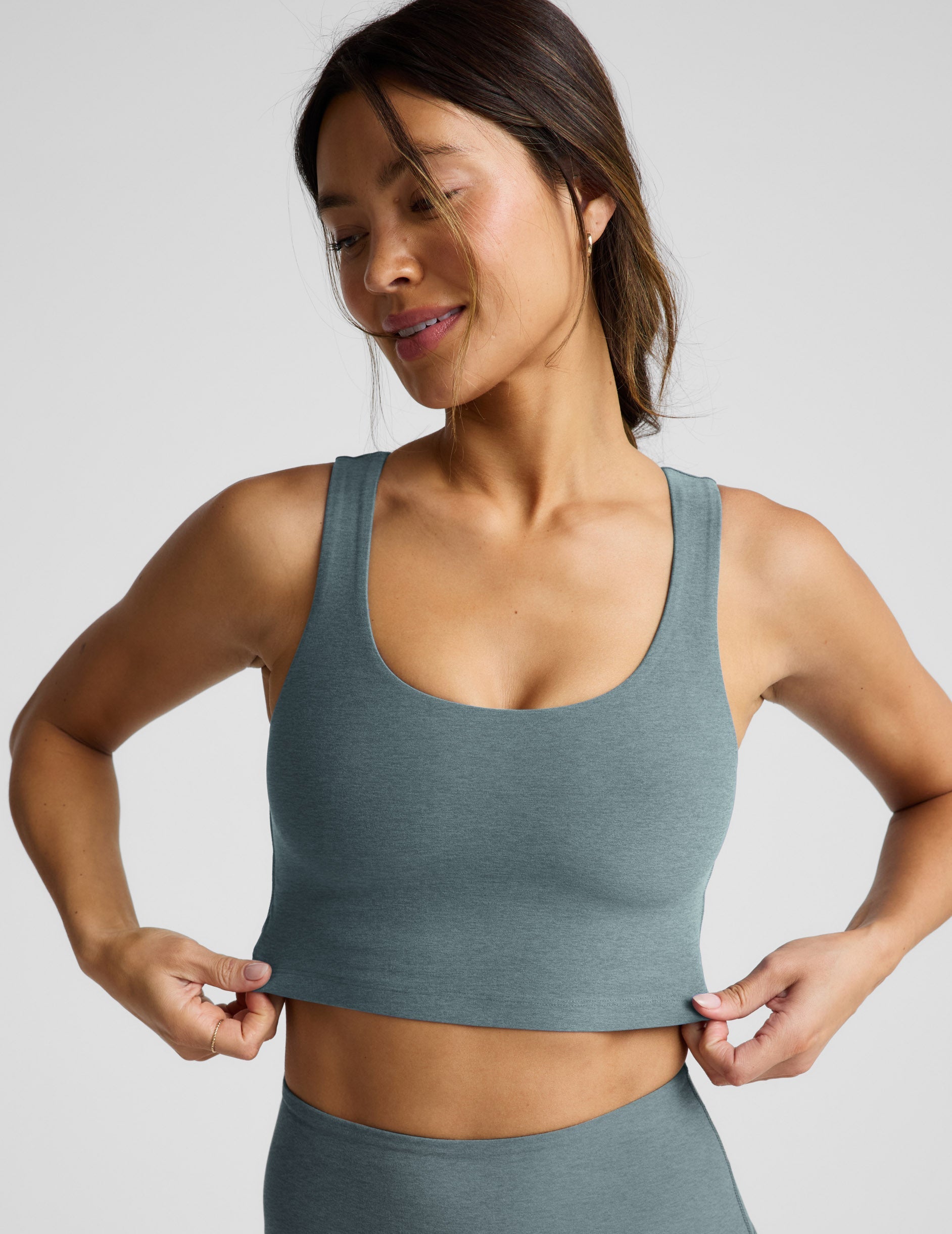 Woman wearing a green cropped tanks and leggings on a light gray background.