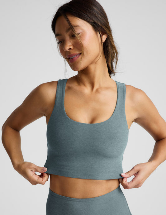 Woman wearing a green cropped tanks and leggings on a light gray background.