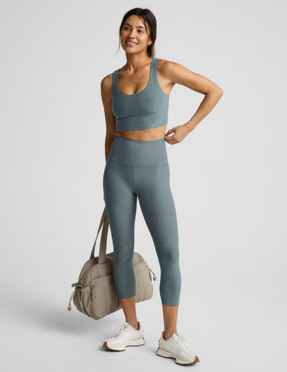 Woman wearing a green cropped tanks and leggings on a light gray background.