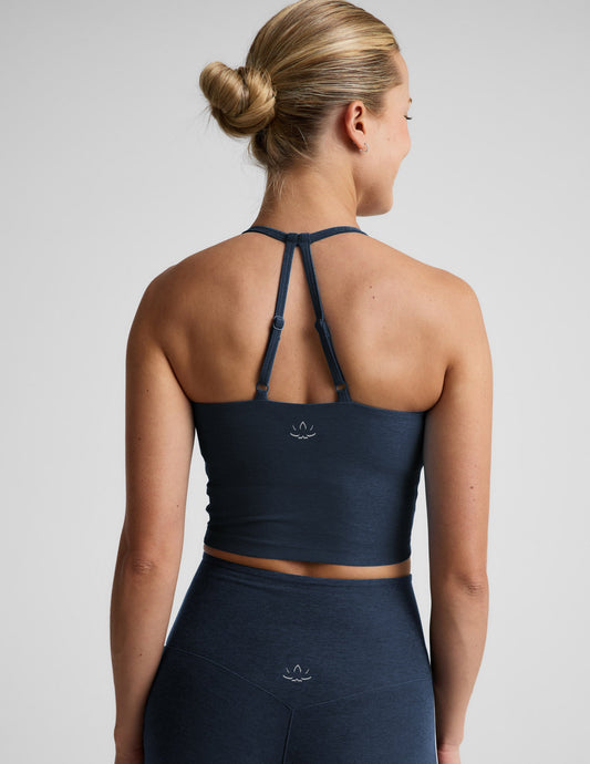 Woman wearing a navy blue strappy cropped tank and leggings against a plain background.