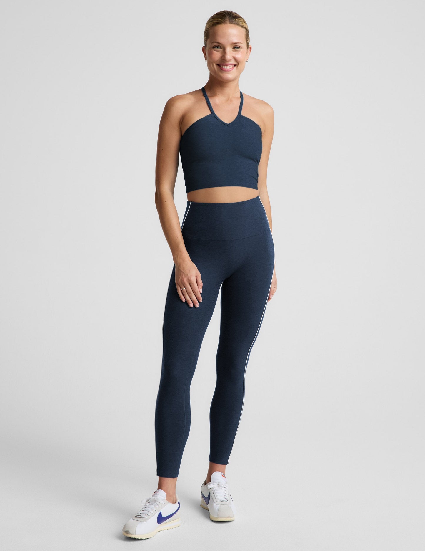 Woman wearing a navy blue strappy cropped tank and leggings against a plain background.