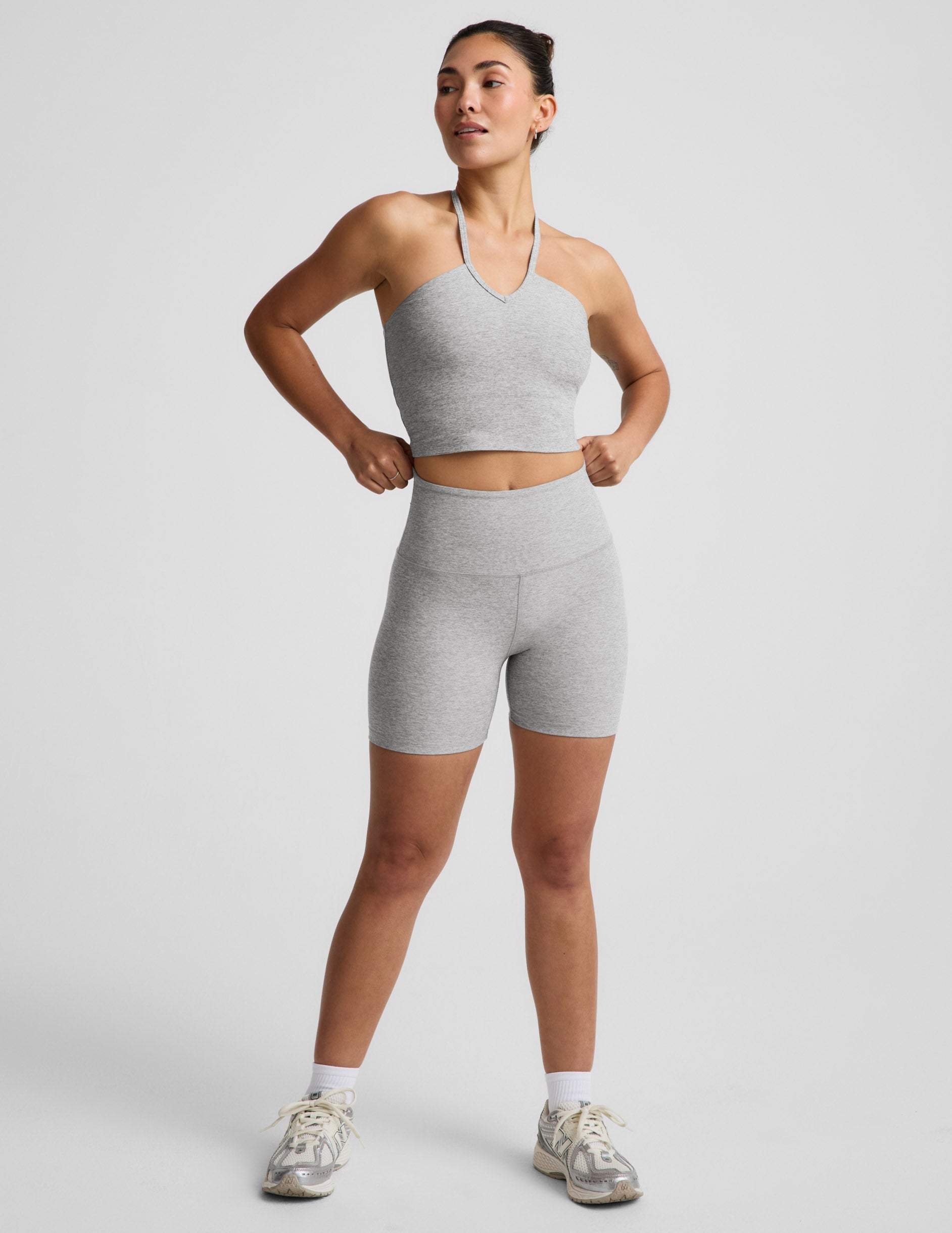 Woman wearing a gray strappy cropped tank and biker shorts against a plain background.