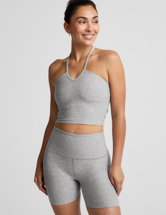 Woman wearing a gray strappy cropped tank and biker shorts against a plain background.