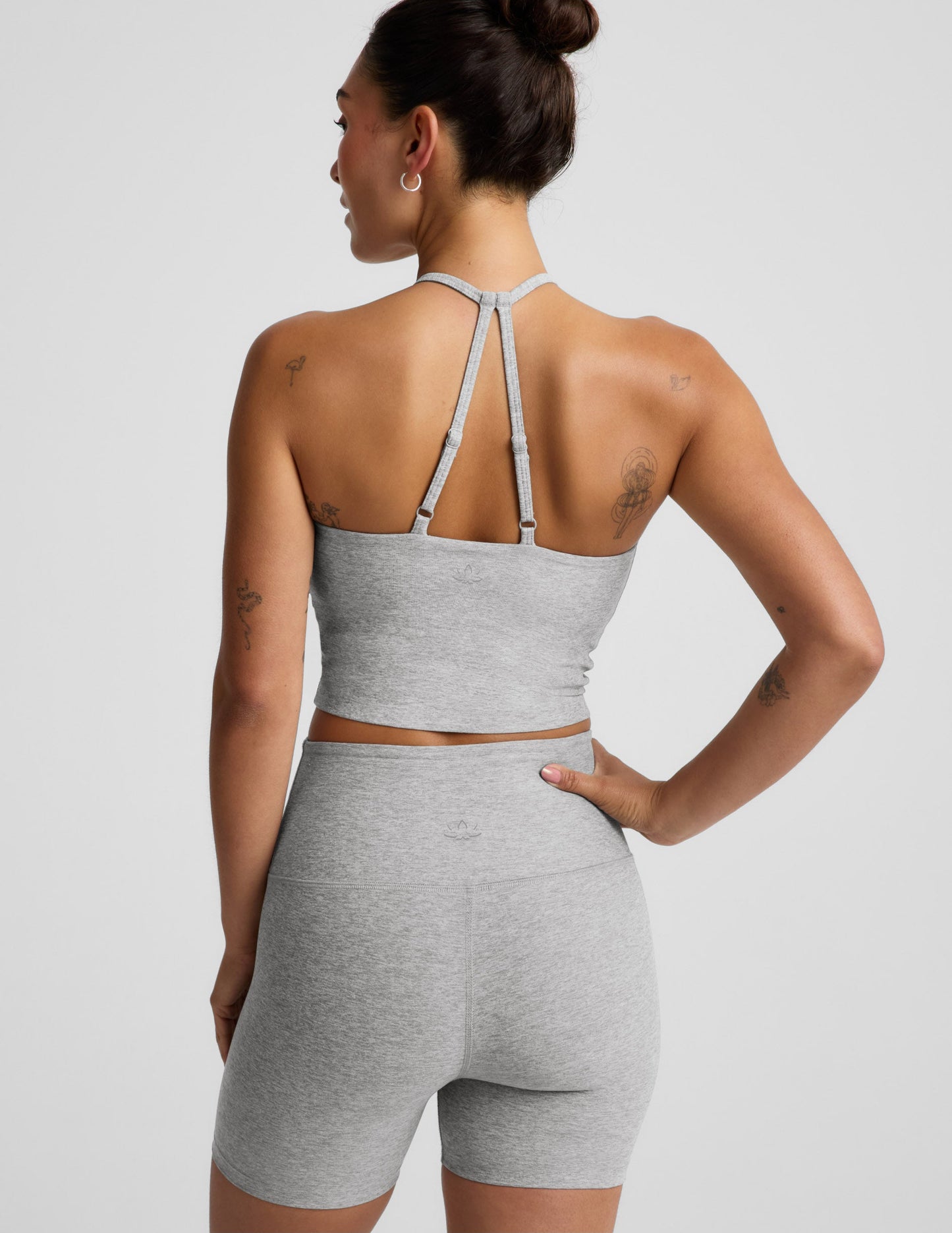 Woman wearing a gray strappy cropped tank and biker shorts against a plain background.