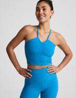 Woman wearing a strappy cropped tank and leggings against a plain background.