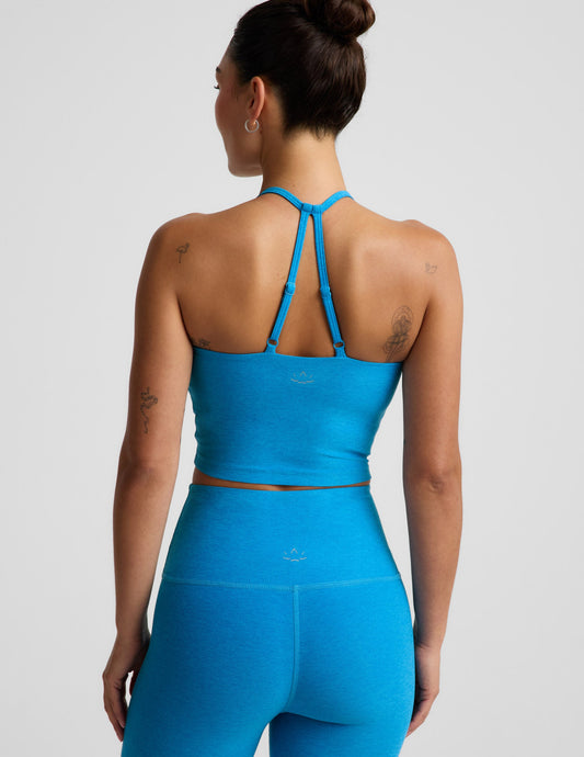 Woman wearing a strappy cropped tank and leggings against a plain background.