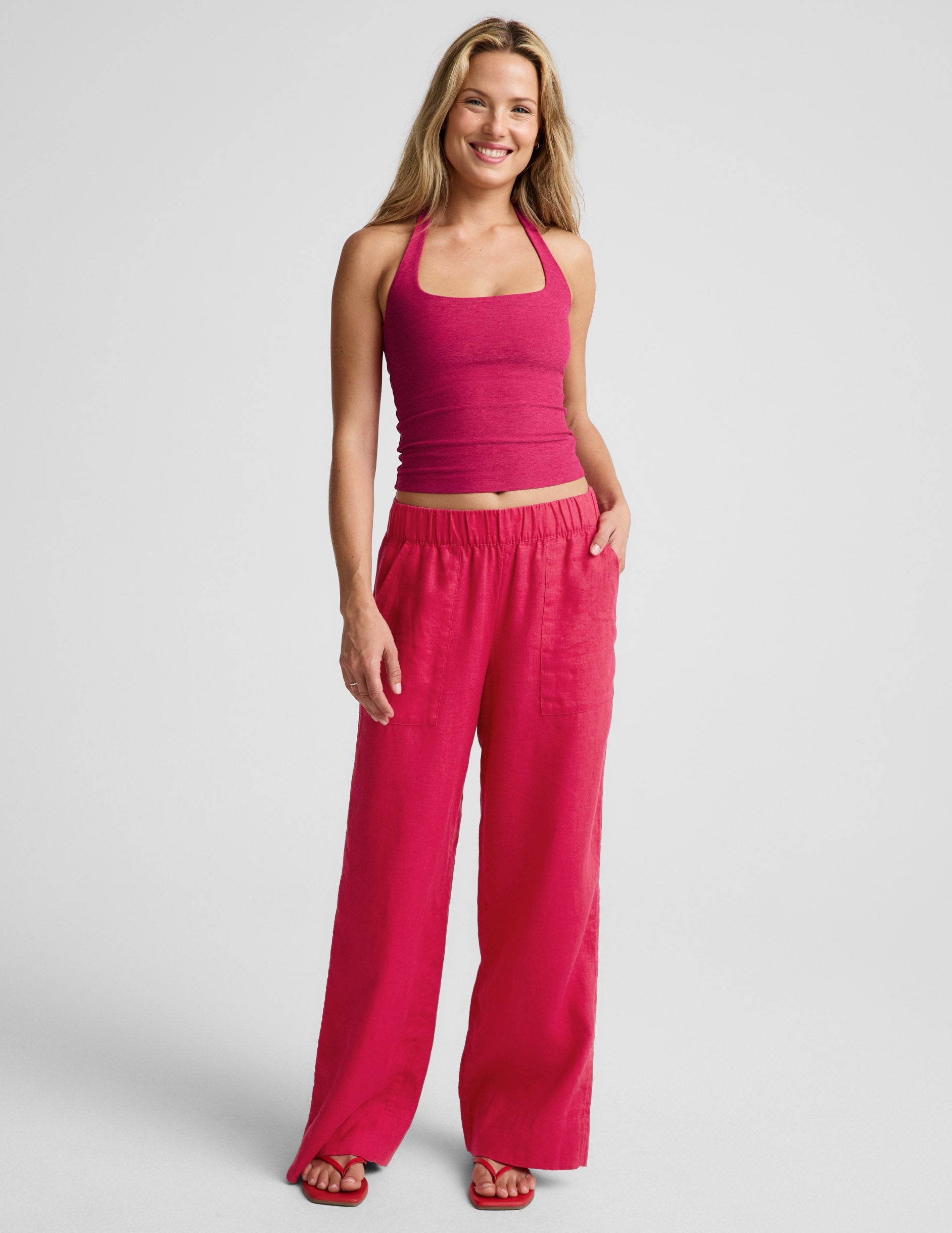 Woman wearing a red halter top and red linen pants against a plain background.