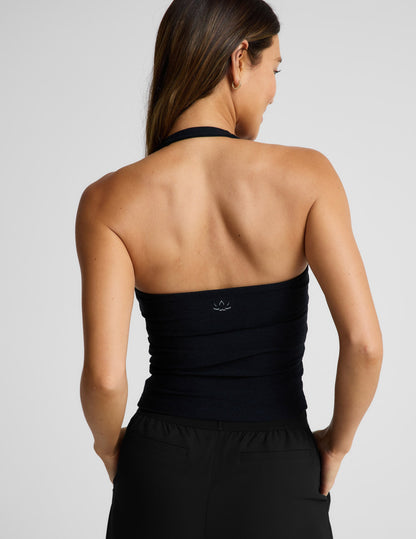 Woman wearing a black halter tank and black pants against a plain background.