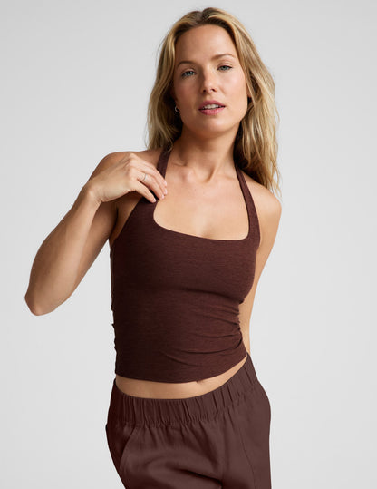 Woman wearing a brown halter tank top and brown linen pants against a plain background.